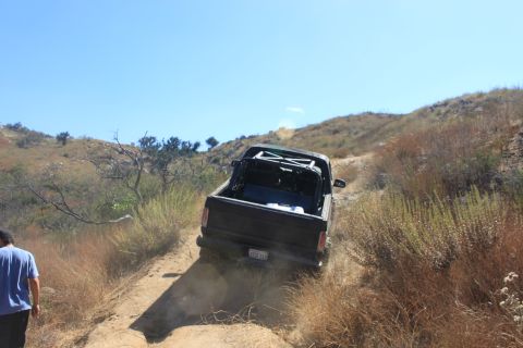 1992 Ford Bronco - Pickup truck navigates a steep, dry, off-road trail under a clear blue sky.