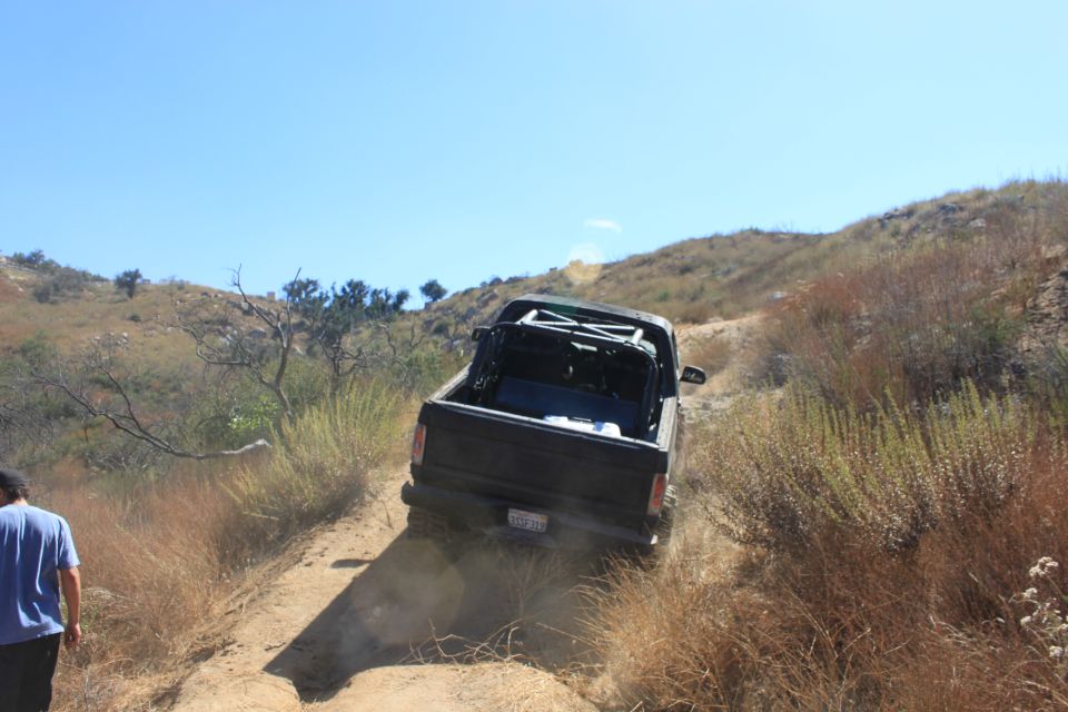 Black pickup truck with roll cage in bed driving up a dusty hill