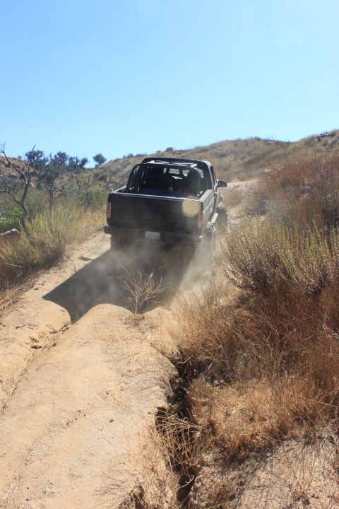1992 Ford Bronco - A black truck kicks up dust as it drives along a dry, rutted dirt path on a sunny day.