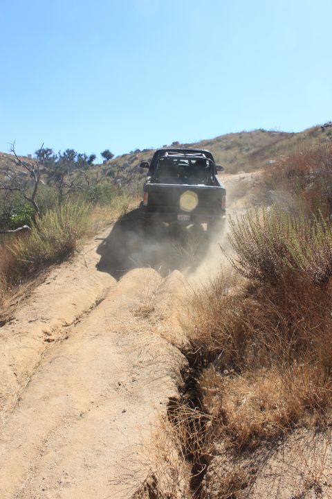 1992 Ford Bronco - A dark SUV navigates a dusty, off-road trail with dry brush on either side.