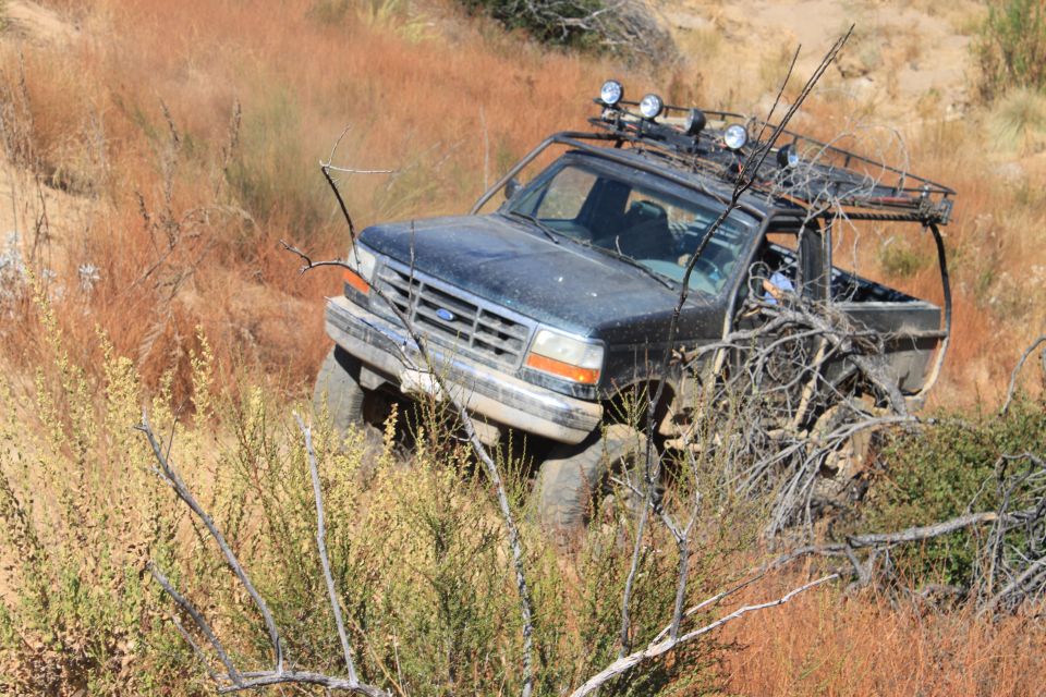 Dark blue 1992 Ford Bronco with roof rack and off-road lights navigating a steep, dry hillside