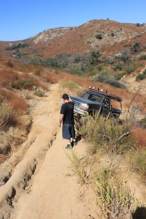 1992 Ford Bronco - An off-road vehicle navigates a challenging dirt path in a dry, hilly landscape under a clear blue sky.