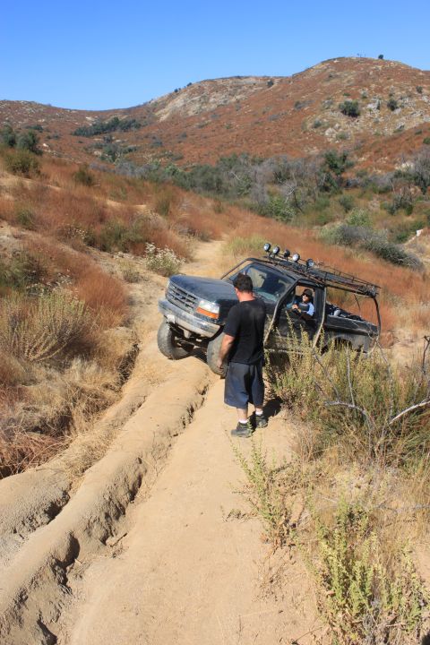 1992 Ford Bronco - A 1992 Ford Bronco navigates a steep, rutted dirt path in a dry, hilly landscape.