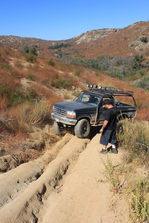 1992 Ford Bronco - A dark 1992 Ford Bronco navigates a dirt trail, with a man observing its progress.