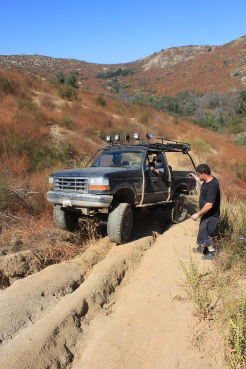 1992 Ford Bronco - 1992 Ford Bronco navigates a challenging off-road trail in a dry, hilly landscape.