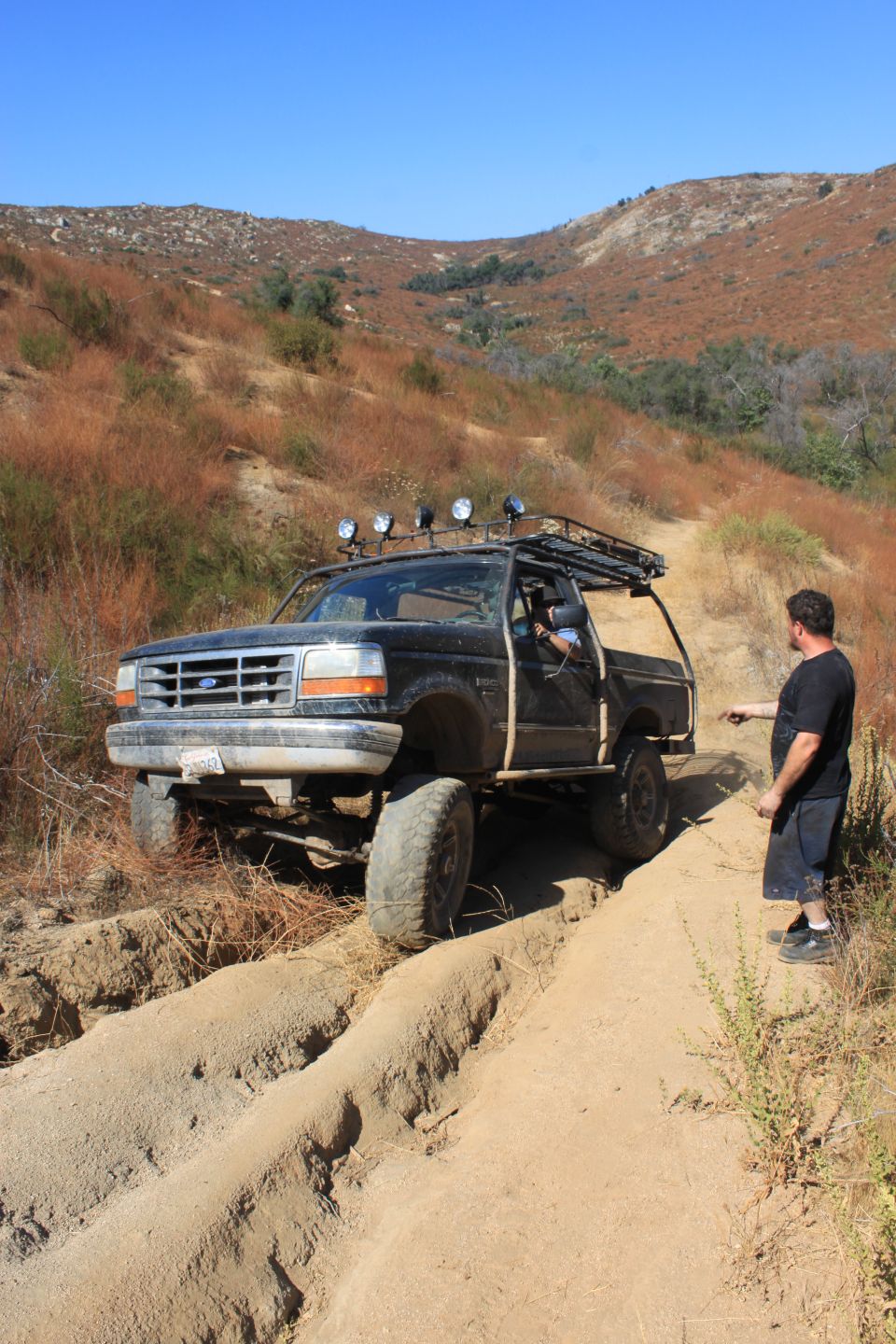 Black Ford F-Series truck with roof rack and lights driving on a dirt trail