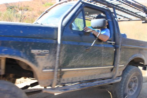 1992 Ford Bronco - A blue Ford Bronco with off-road modifications is driven on a dirt path.