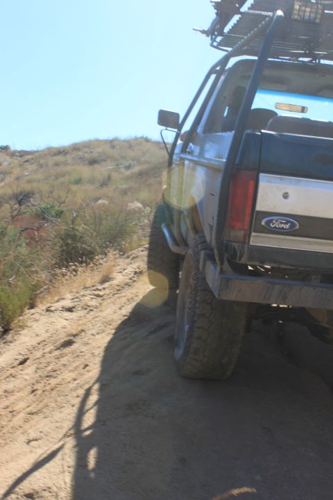 1992 Ford Bronco - 1992 Ford Bronco driving on a dusty trail with a roof rack visible.