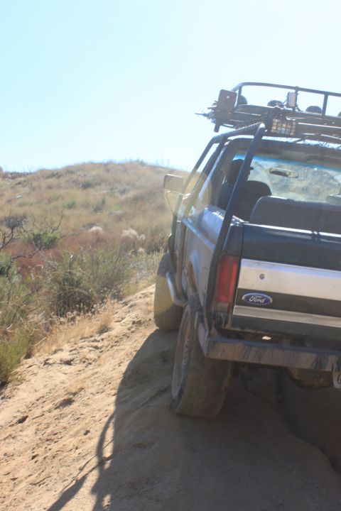 1992 Ford Bronco - This Ford Bronco is navigating a dusty, off-road trail under a clear blue sky.