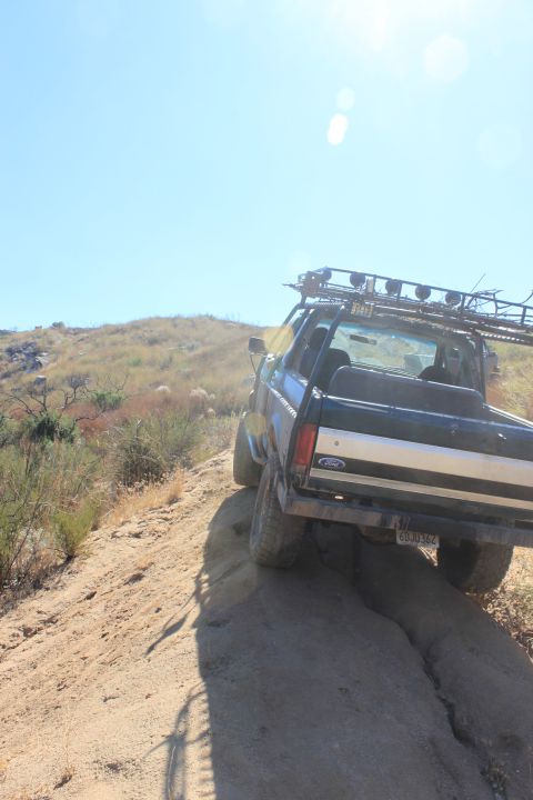 1992 Ford Bronco - A black 1992 Ford Bronco navigates a rough dirt path under a clear blue sky.