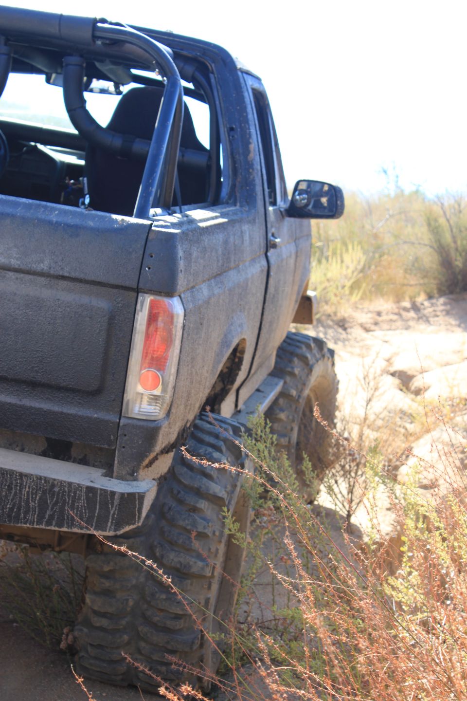 1992 Ford Bronco with roll cage and large tires on a dirt trail
