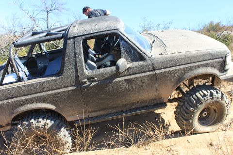 1992 Ford Bronco - This heavily modified SUV is covered in mud and navigating a challenging off-road course.