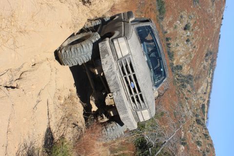1992 Ford Bronco - A gray 1992 Ford Bronco navigates a challenging dirt trail, tilted precariously on the incline.