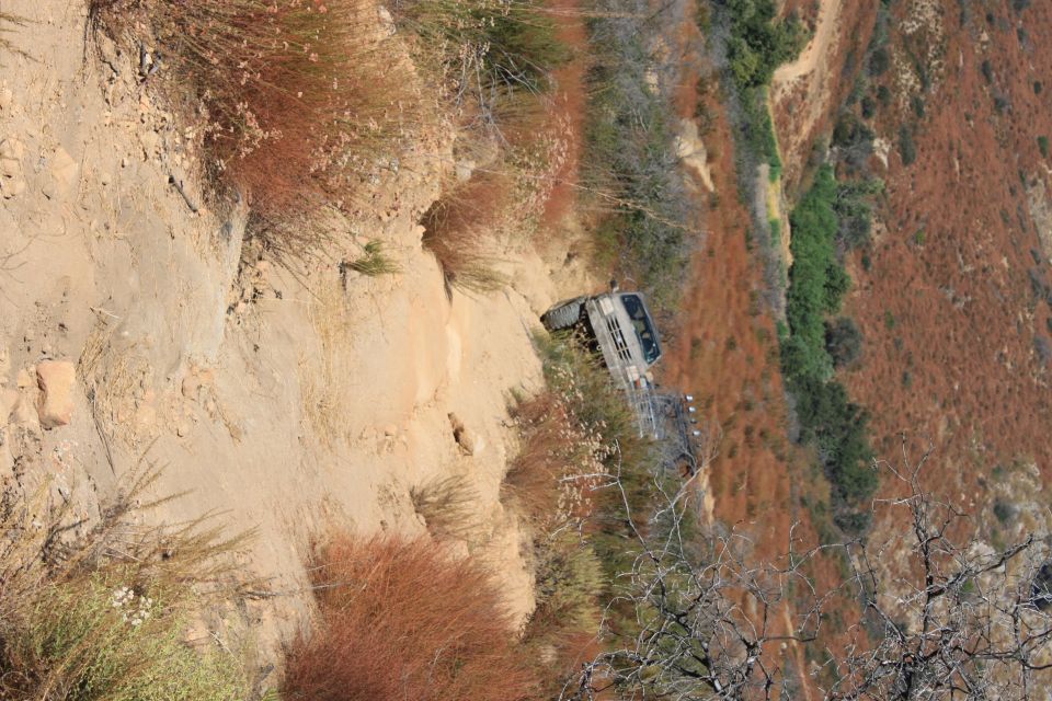 1992 Ford Bronco navigating a narrow, steep dirt trail with dry brush on either side