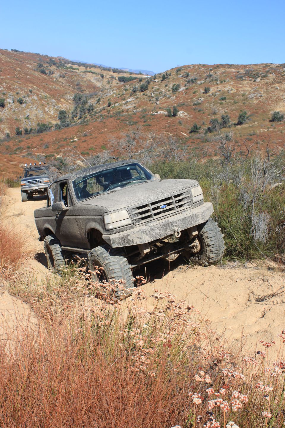 Gray Ford F-Series truck on a dirt trail, front wheel deep in sand, lifted suspension, off-road tires