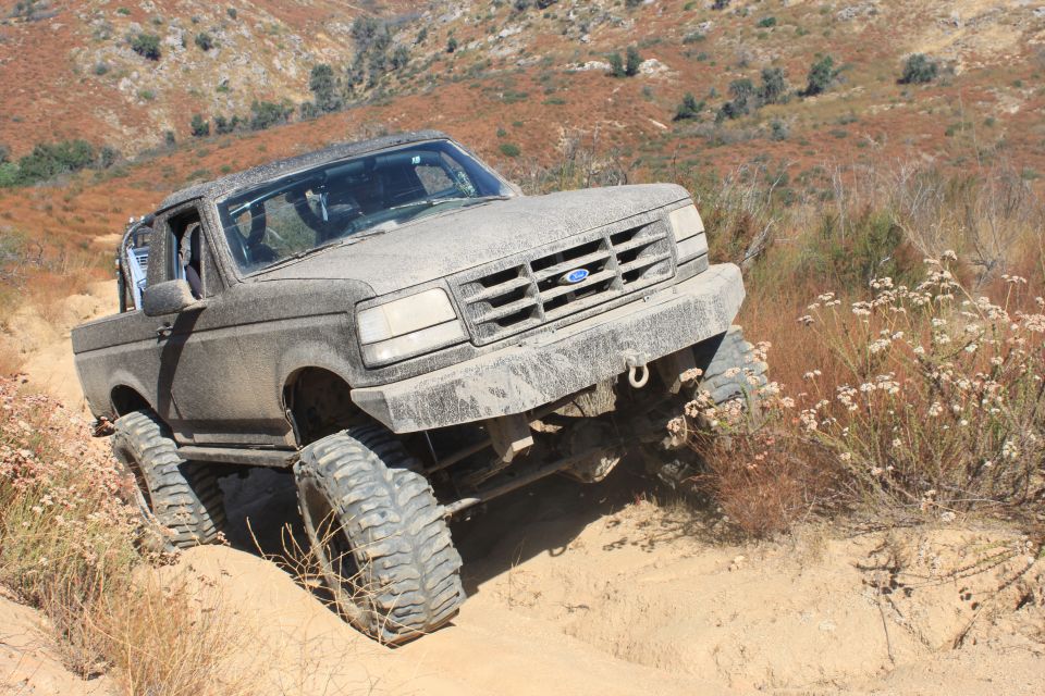 1992 Ford Bronco climbing a dirt trail, covered in mud