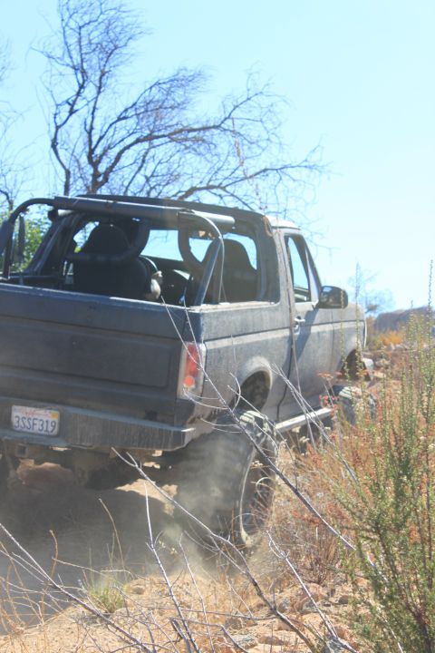 1992 Ford Bronco - This SUV is navigating a dusty, off-road trail with sparse vegetation and clear blue skies.