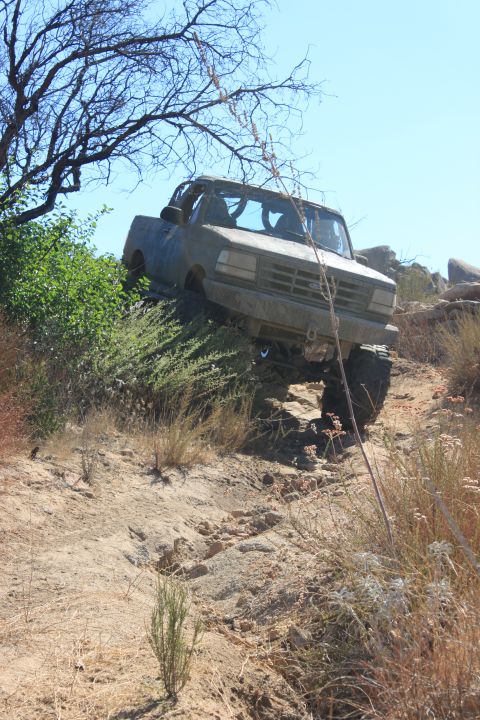 1992 Ford Bronco - An off-road truck navigates a challenging, rocky trail under a clear blue sky.
