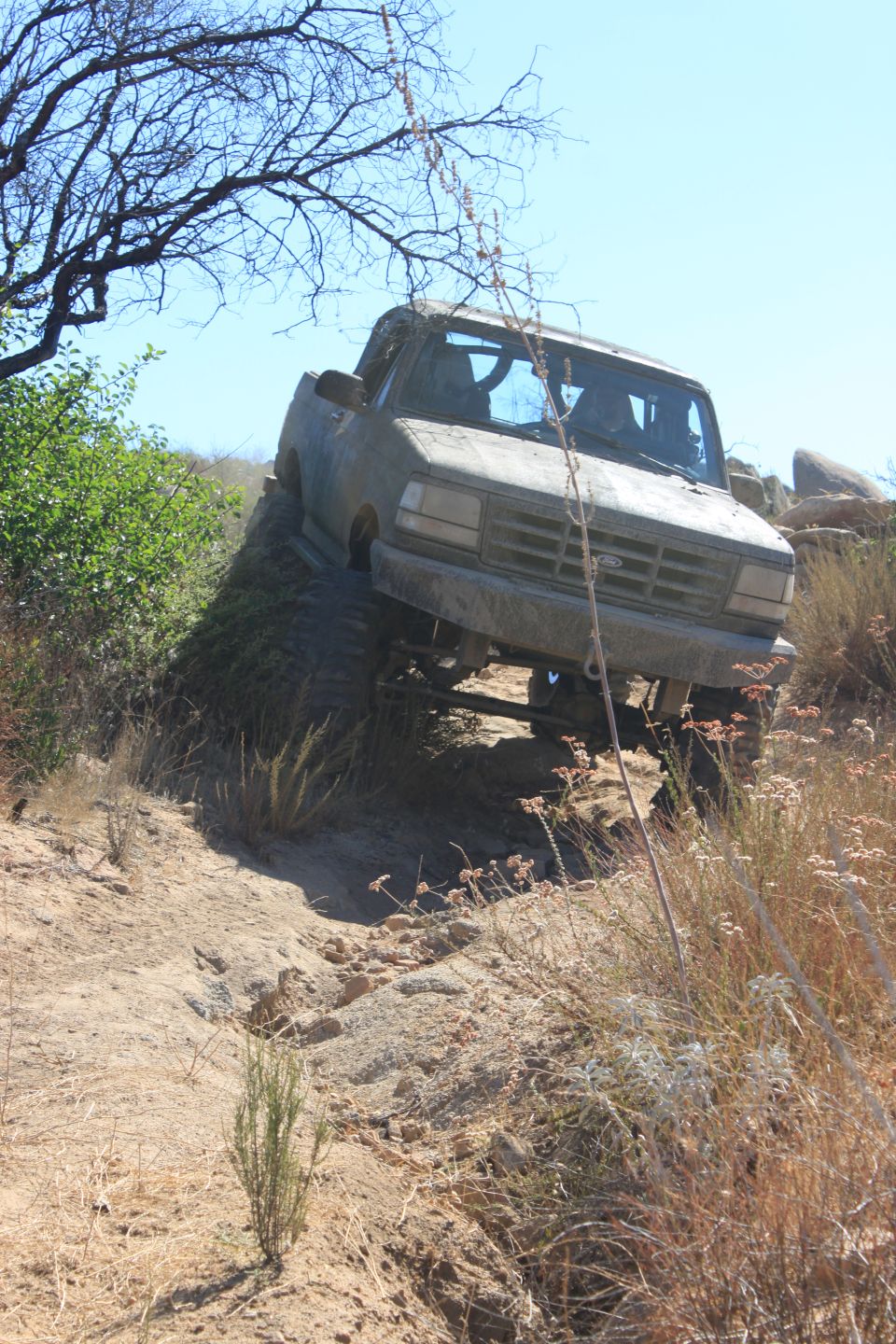 1992 Ford Bronco climbing a steep dirt embankment with dry brush and rocks