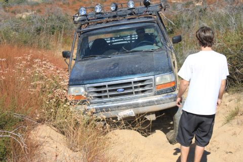 1992 Ford Bronco - A 1992 Ford Bronco navigates a rough, dry terrain with a person standing nearby.