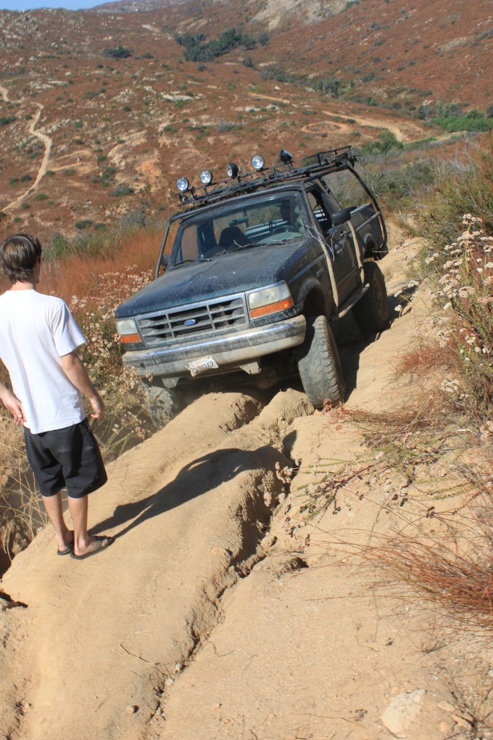 1992 Ford Bronco on a steep dirt trail with a person watching