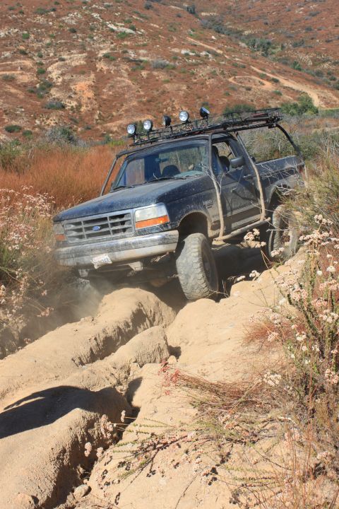 1992 Ford Bronco - A black 1992 Ford Bronco tackles a challenging off-road trail, kicking up dust as it goes.