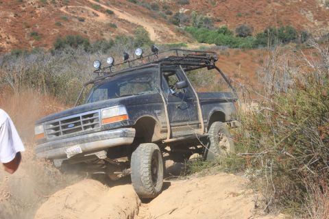 1992 Ford Bronco - This 1992 Ford Bronco navigates a challenging dirt path, equipped with a heavy-duty roof rack and off-road lights.