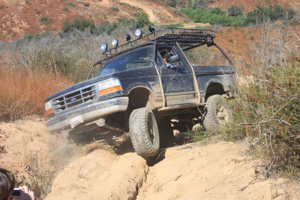 1992 Ford Bronco climbing a steep dirt hill with off-road lights and roof rack