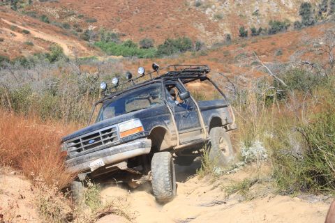 1992 Ford Bronco - A 1992 Ford Bronco navigates a challenging off-road trail with steep inclines and dry vegetation.