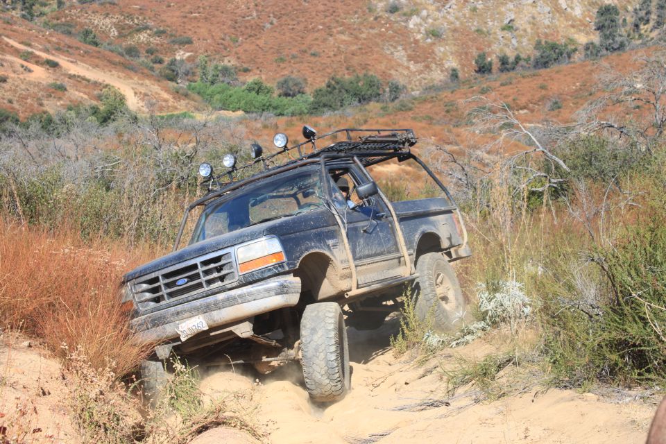 Ford Bronco climbing a dirt hill with a roof rack and off-road lights