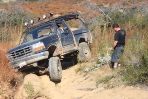 1992 Ford Bronco - A black 1992 Ford Bronco navigates a challenging off-road trail, with a man observing the action from the side.