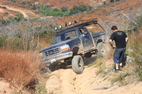 1992 Ford Bronco - A man watches a 1992 Ford Bronco navigate a steep, sandy trail in a dry, brushy environment.