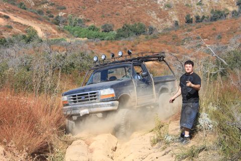 1992 Ford Bronco - A black 1992 Ford Bronco navigates a dusty off-road trail with a man standing nearby.