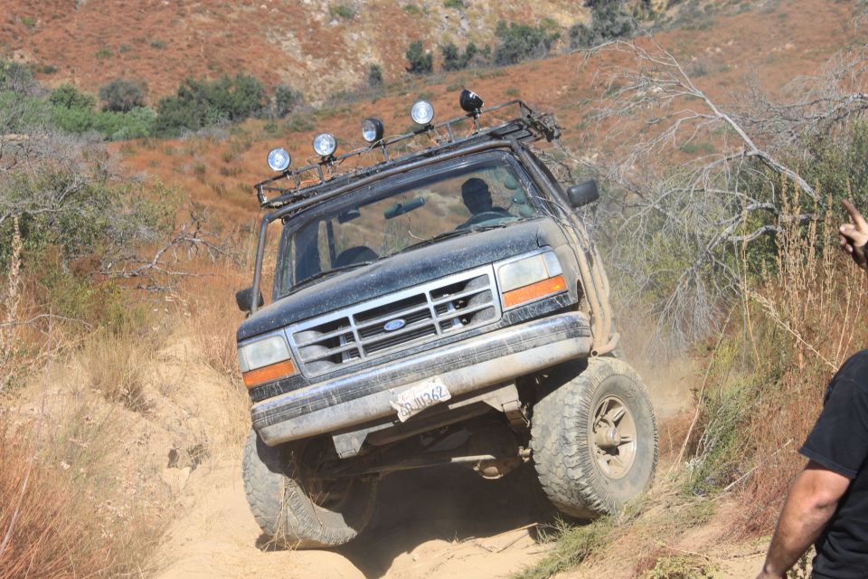 1992 Ford Bronco with roof lights navigating a steep dirt trail, front grille visible
