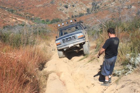 1992 Ford Bronco - A man observes a 1992 Ford Bronco navigating a challenging off-road trail.