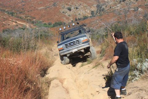 1992 Ford Bronco - A 1992 Ford Bronco navigates a challenging dirt trail with a man observing the action.