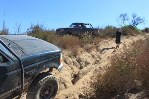 1992 Ford Bronco - Two off-road vehicles navigate a challenging dirt trail under a clear blue sky.