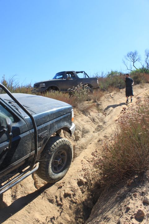 1992 Ford Bronco - Two trucks navigate a challenging off-road trail under a clear blue sky.