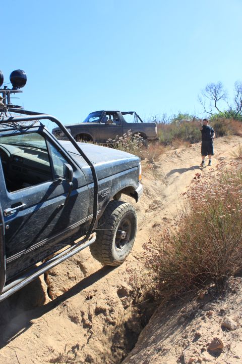 1992 Ford Bronco - Two trucks navigate a challenging off-road trail under a clear blue sky.