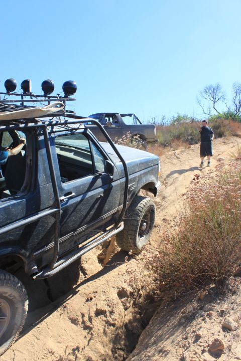 1992 Ford Bronco - Two off-road vehicles are seen on a challenging dirt trail under a clear blue sky.