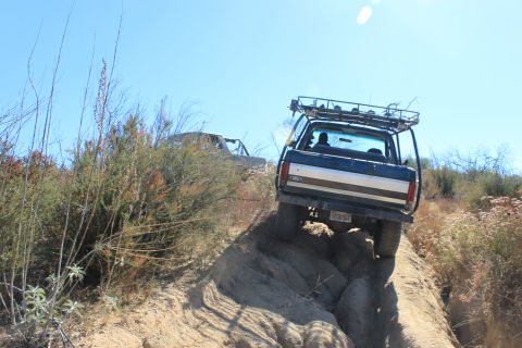 1992 Ford Bronco - Two off-road vehicles ascend a challenging, sun-drenched trail with dry brush.