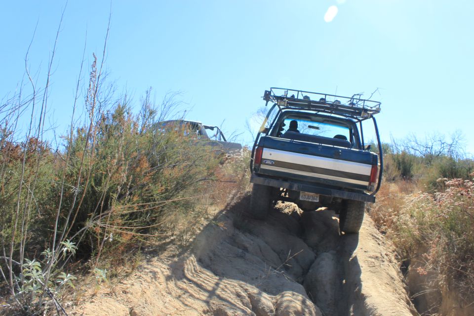 Dark blue Ford Bronco with a roof rack navigates a steep, rocky incline