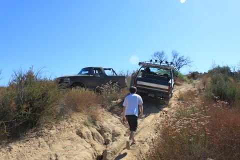 1992 Ford Bronco - Two SUVs navigate a steep, dusty trail under a clear blue sky, with one vehicle appearing to be a 1992 Ford Bronco.