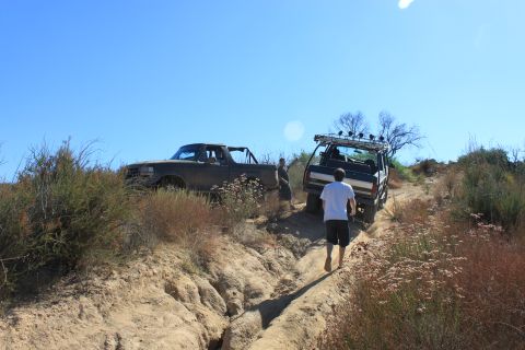 1992 Ford Bronco - Two off-road vehicles navigate a challenging dirt trail under a clear blue sky.