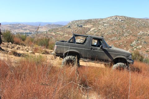 1992 Ford Bronco - A 1992 Ford Bronco navigates a dry, grassy hillside under a clear blue sky.