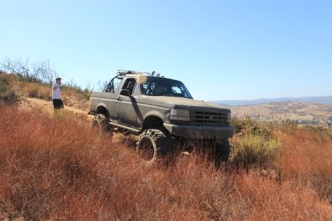 1992 Ford Bronco - Modified 1992 Ford Bronco navigates an off-road trail under a clear blue sky.