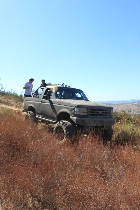 1992 Ford Bronco - A modified 1992 Ford Bronco navigates a dry, grassy trail under a clear blue sky.
