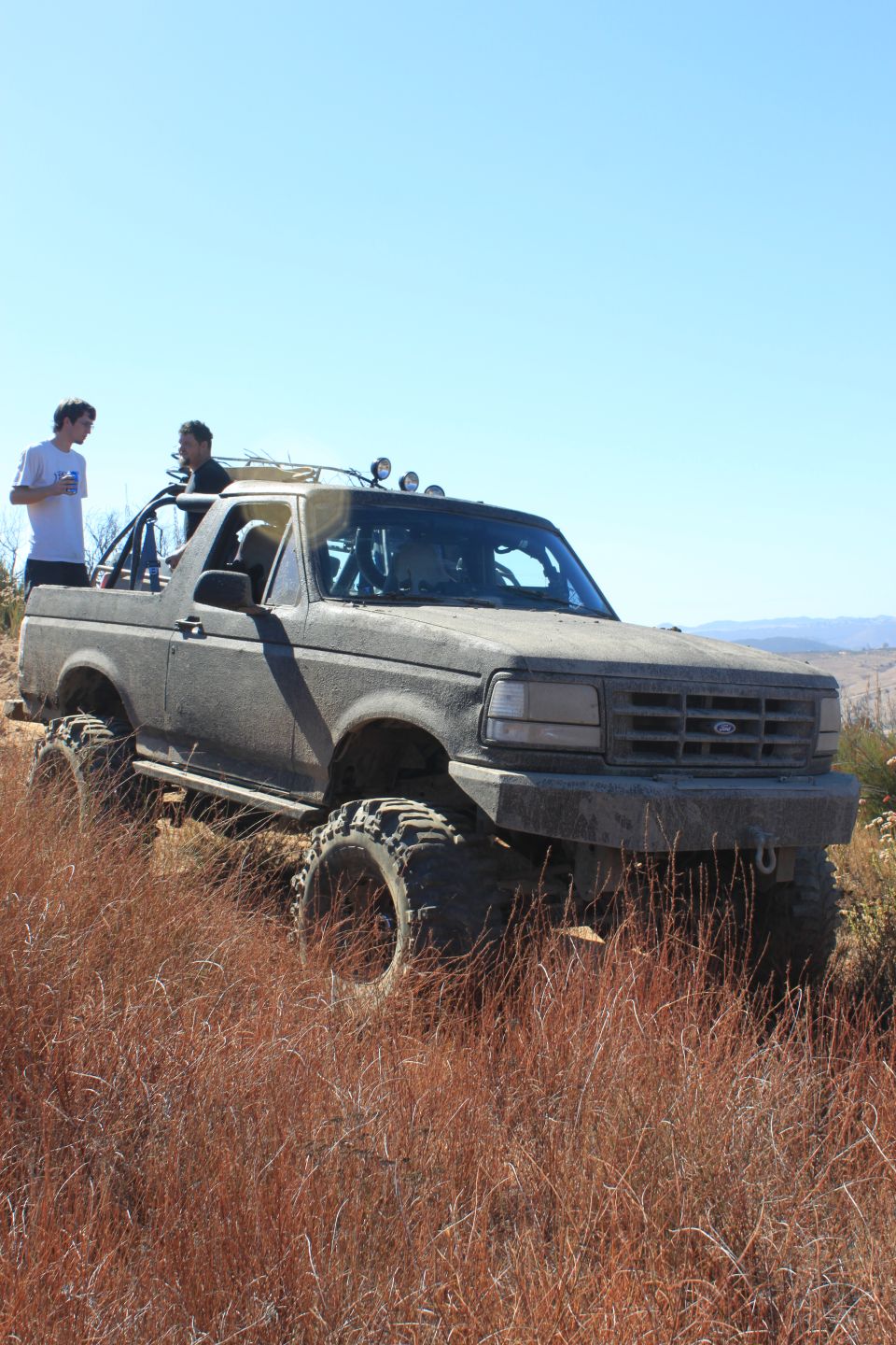 1992 Ford Bronco on a dry, grassy hill with two people standing in it