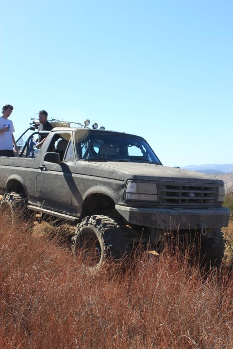 1992 Ford Bronco - Modified 1992 Ford Bronco navigates rough terrain under a clear blue sky.
