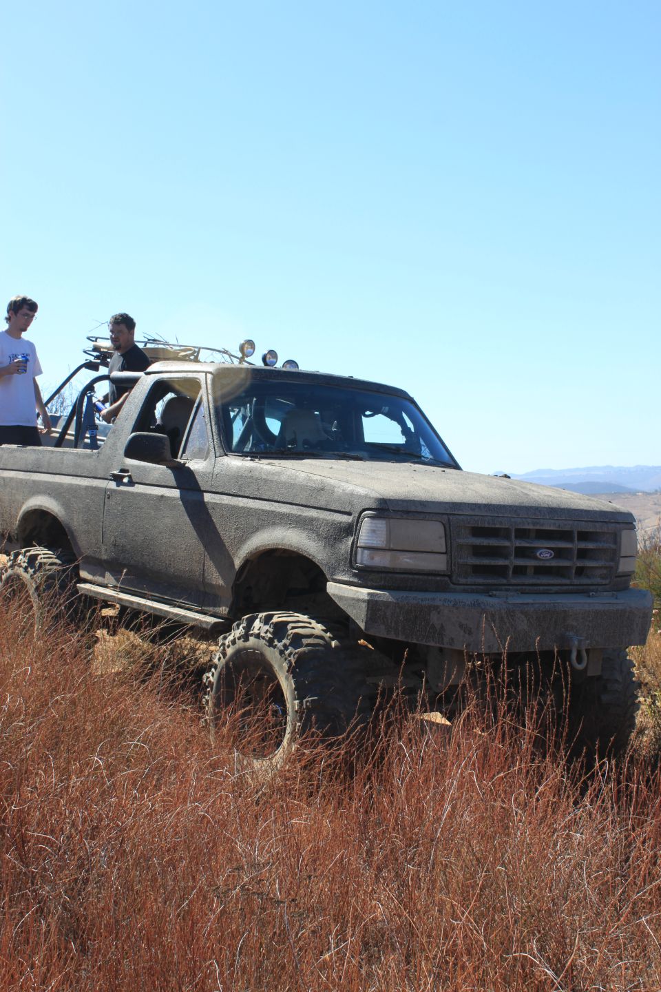 1992 Ford Bronco with large tires on a dry, grassy hill with two people in it